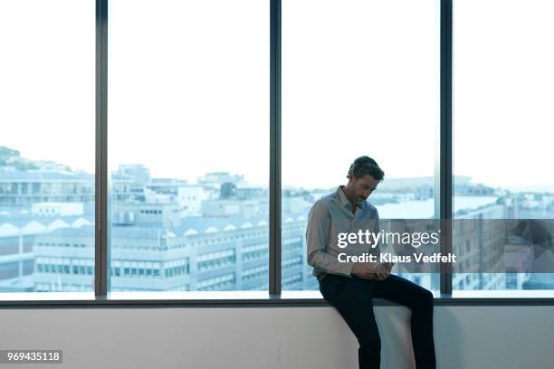 businessman sitting in big windows in office space, checking smartphone - luxury city break stock pictures, royalty-free photos & images