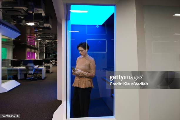 young businesswoman checking smartphone in "phone booth" in corporate office space - telephone box stock pictures, royalty-free photos & images