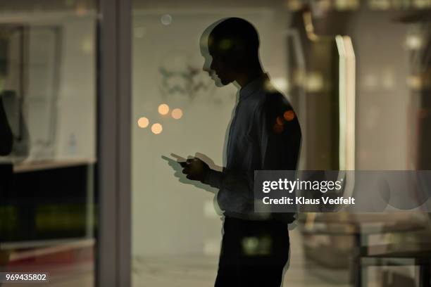 reflection of young businessman checking phone inside office at nighttime - double exposure business stockfoto's en -beelden