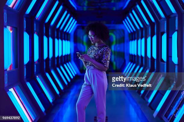 young businesswoman looking at smartphone in spaceship like corridor - tecnologia fotografías e imágenes de stock