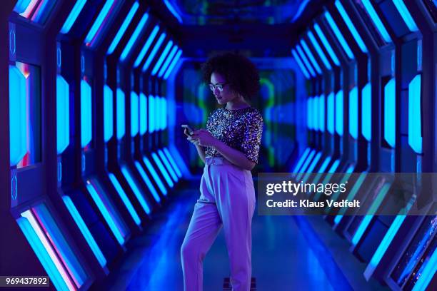 young businesswoman looking at smartphone in spaceship like corridor - digitale technologie stockfoto's en -beelden