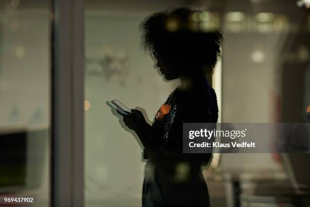 reflection of young businesswoman checking smartphone in the office at night - girl silhouette stockfoto's en -beelden