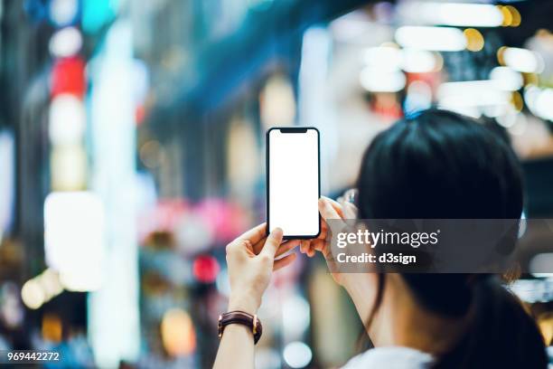 woman capturing city street scene with smartphone against illuminated street lights - woman capturing city night foto e immagini stock