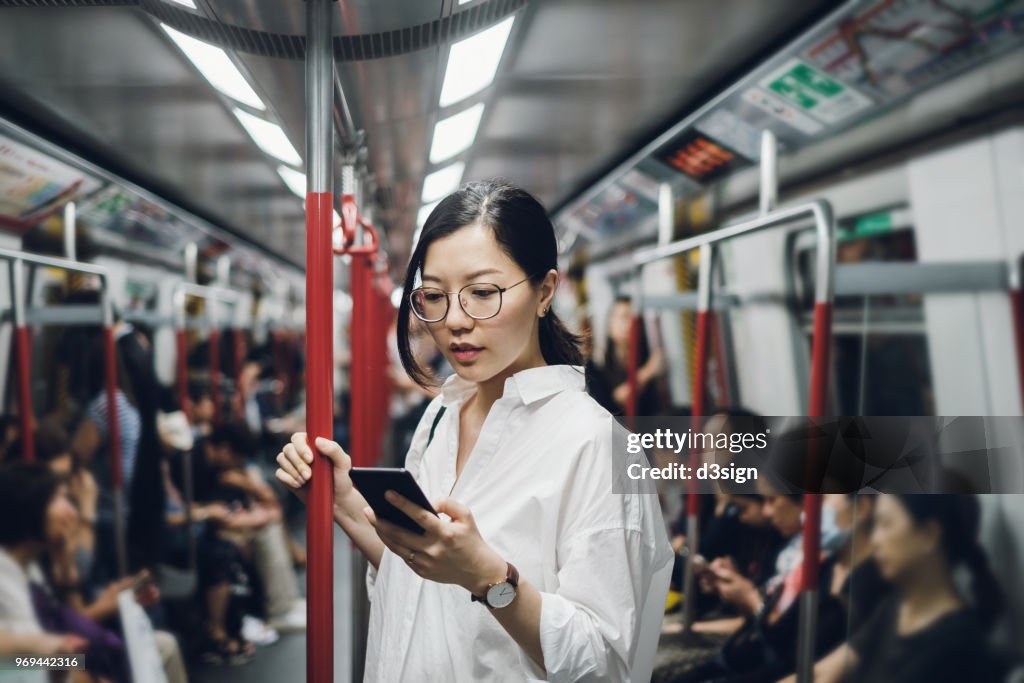 Young businesswoman looking at smartphone while riding on subway