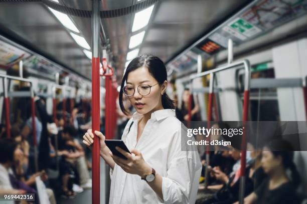 young businesswoman looking at smartphone while riding on subway - hora de ponta papel humano imagens e fotografias de stock