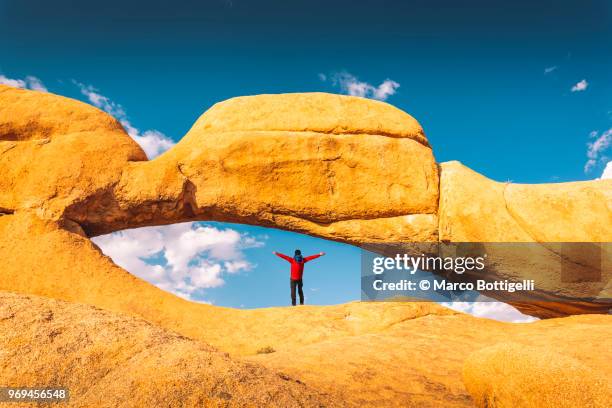 tourist with outstretched arms at spitzkoppe big arch, namibia - spitzkoppe stock pictures, royalty-free photos & images