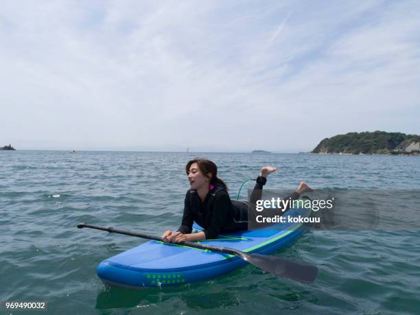 una donna è sdraiata su una tavola in supplica. - surf board foto e immagini stock