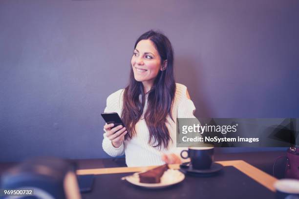 beautiful black hair woman in white sweater, sitting in cafe, drinking coffee, using mobile phone - no drinking stock pictures, royalty-free photos & images