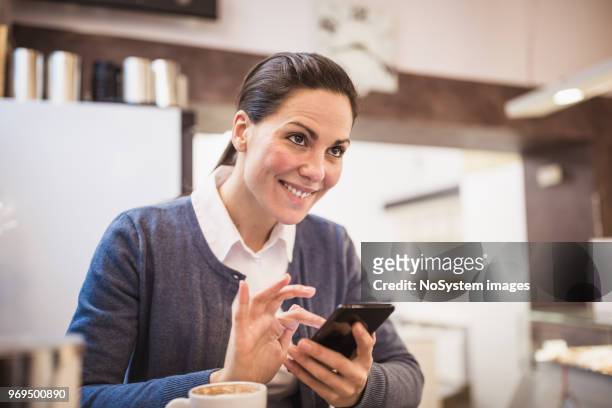 young woman drinking coffee, using mobile phone, sitting in cafe - no drinking stock pictures, royalty-free photos & images
