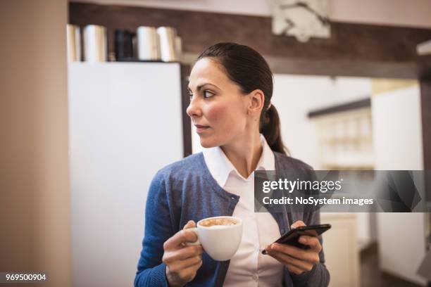 young woman drinking coffee, using mobile phone, sitting in cafe - no drinking stock pictures, royalty-free photos & images