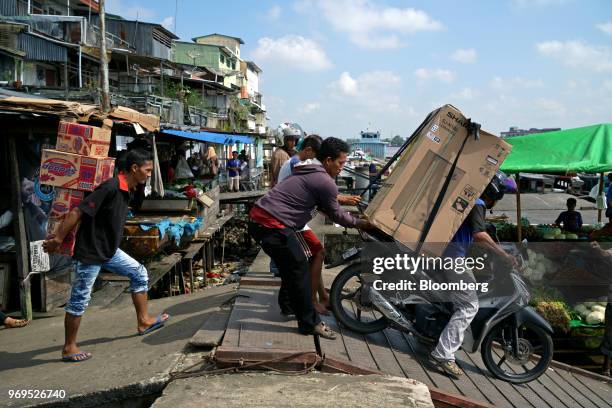 People assist a man transporting a fridge on a motorcycle at a dock along the Kapuas river in Pontianak, in West Kalimantan, Indonesia, on Saturday,...