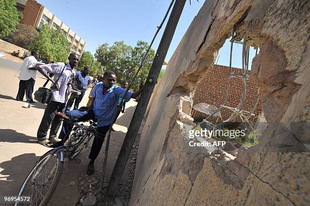People look through a hole left by an explosion at the office of a state mediator on February 22, 2010 in Niamey few days after the coup that...