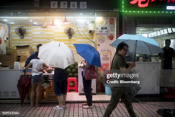 Woman with an umbrella walks past customers at a fruit juice vendor in Shenzhen, China, on Thursday, June 7, 2018. China's efforts to connect the...