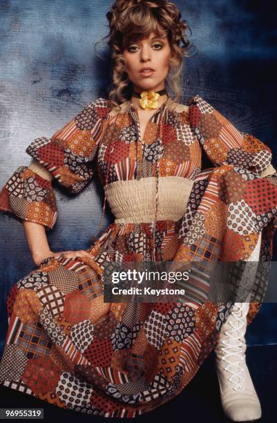 Model wearing a patchwork pattern dress with white laced boots, circa 1975.