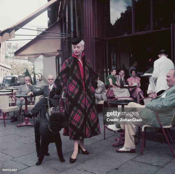 Woman wearing a tartan winter coat and black pillbox hat draws glances from the patrons of a pavement cafe, 1952. Original Publication: Picture Post...
