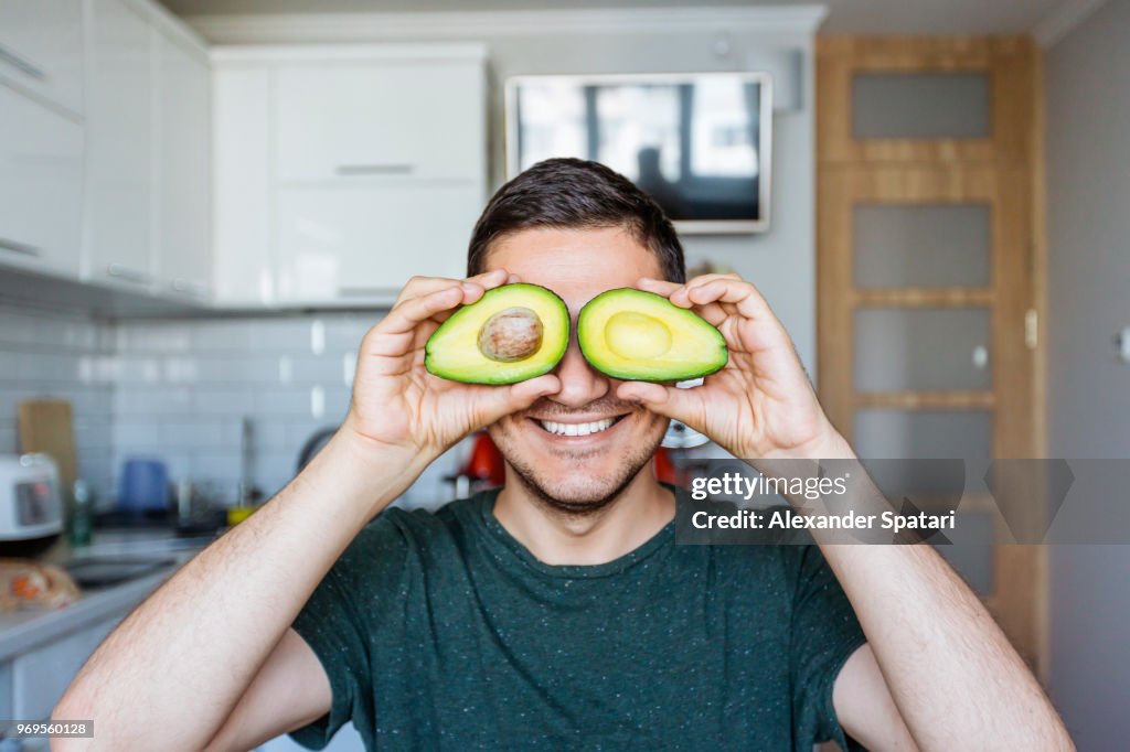 Young man having fun with avocado at the kitchen