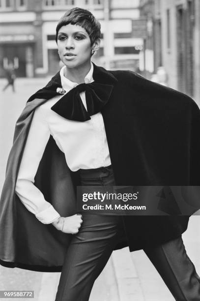 Fashion model Sonia Pugin wearing high waist trousers, white shirt with black ribbon and cape, UK, 25th April 1967.