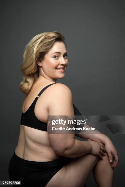 plus size woman in her thirties wearing only black lingerie sitting in front of a dark gray background while looking over her shoulder with a big smile. - buxom blonde fotografías e imágenes de stock