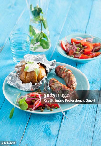 sausages wrapped in parma ham with sage served with a tomato salad and a baked potato - tillbehörssallad bildbanksfoton och bilder