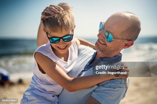 vater mit sohn am strand spielen - eltern sonnenbrille sonne lachen stock-fotos und bilder