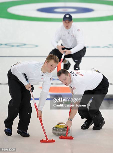 John Benton and Jeff Isaacson of the United States brush the ice backdropped by their skip John Shuster during the men's curling round robin game...