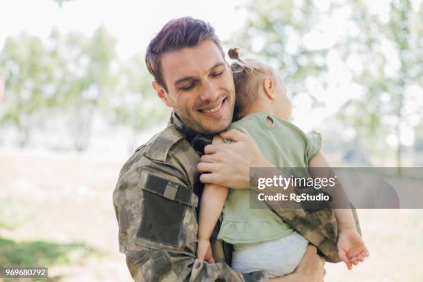 soldaat glimlachend en knuffelen met zijn baby dochter - baby being held stockfoto's en -beelden