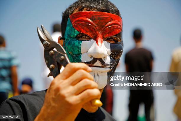 Palestinian protestor wearing a Guy Fawkes mask coloured with the Palestinian flag poses while holding a wirecutter on June 8, 2018 during a...