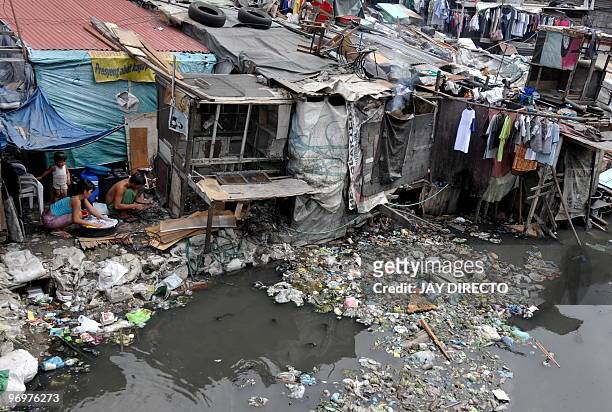 Woman washes laundry with her children beside a cluster of shanties erected on the banks of a polluted creek in Manila on February 17, 2010....