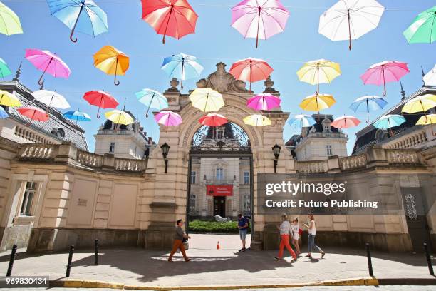 Colourful umbrellas hover above a street near the gates of the Potocki Palace as its facade bears a banner in support of Ukrainian filmmaker Oleh...