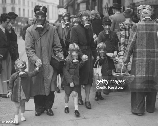 Family wearing their gas masks to the shops during a gas drill in Richmond, Surrey, 31st May 1941. The drill involved a canister of tear gas to...