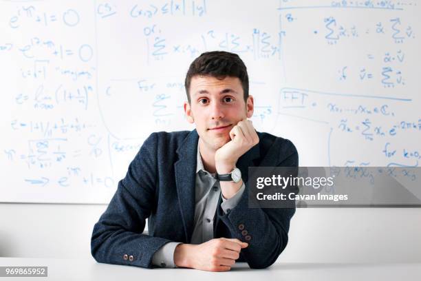 portrait of businessman sitting against whiteboard in office - mano sul mento foto e immagini stock