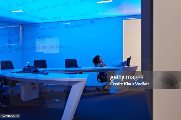 young businesswoman relaxing with feet up, in corporate board room at night - weiblicher teenager allein stock-fotos und bilder