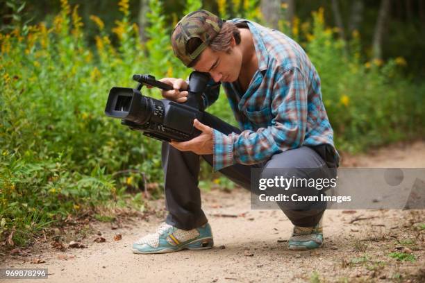man using video camera while crouching on dirt road - cameraman photos et images de collection