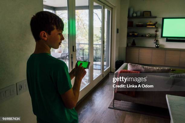 teenage boy holding smart phone with green screen tv in background - lcd tv stock pictures, royalty-free photos & images