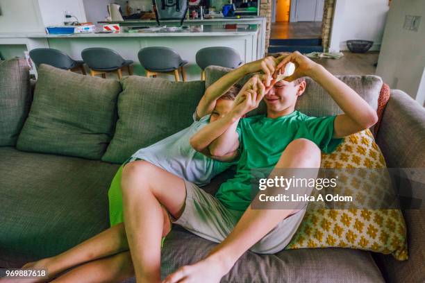 two brothers rough housing on sofa - two boys wrestling stock pictures, royalty-free photos & images