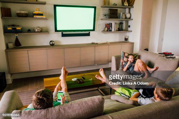 three siblings on living room sofa with green screen tv in background - 液晶テレビ ストックフォトと画像