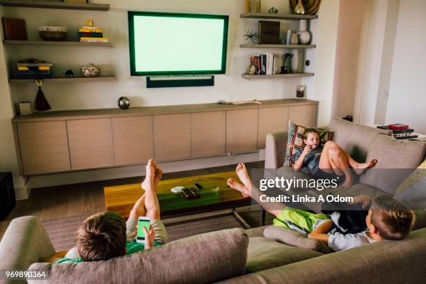 three siblings on living room sofa with green screen tv in background - lcd television stockfoto's en -beelden