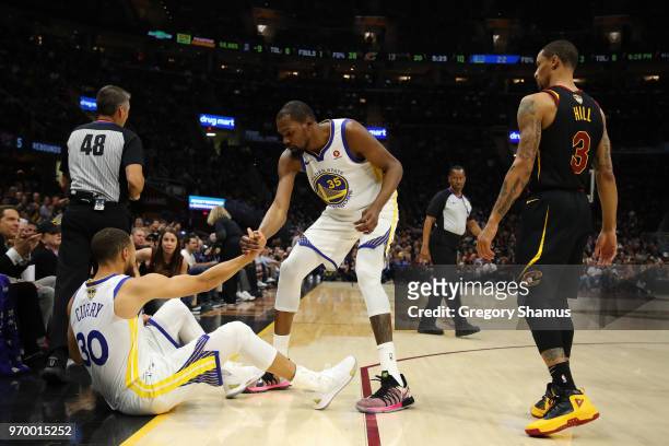 Kevin Durant of the Golden State Warriors helps up Stephen Curry as George Hill of the Cleveland Cavaliers looks on in the first quarter during Game...