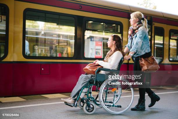 physically handicapped woman in wheelchair gets assistance disabled young woman in wheelchair at railroad track - public transport stock pictures, royalty-free photos & images