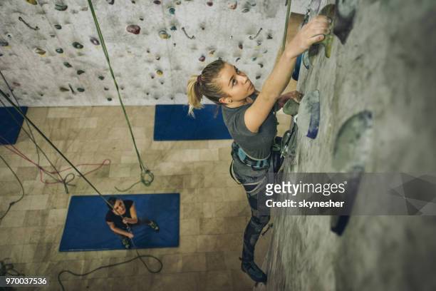 above view of young woman exercising wall climbing in a gym with a help of a coach. - climber stock pictures, royalty-free photos & images