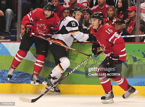 Canadian forward Michael Richards checks Germany's forward Travis Mulock as Canadian forward Jonathan Toews skates past during the Men's Ice Hockey...