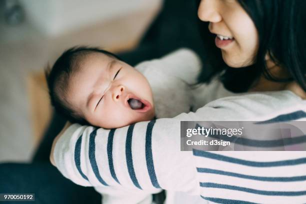 caring asian young mother holding yawning baby in arms with love and smile - baby　smile ストックフォトと画像