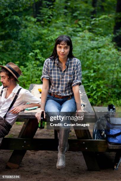 portrait of woman holding beer bottle while sitting with friend on picnic table in forest - cut off flannel shirt stock pictures, royalty-free photos & images