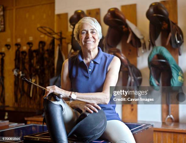 portrait of smiling jockey sitting on table in stable - riding crop stock pictures, royalty-free photos & images