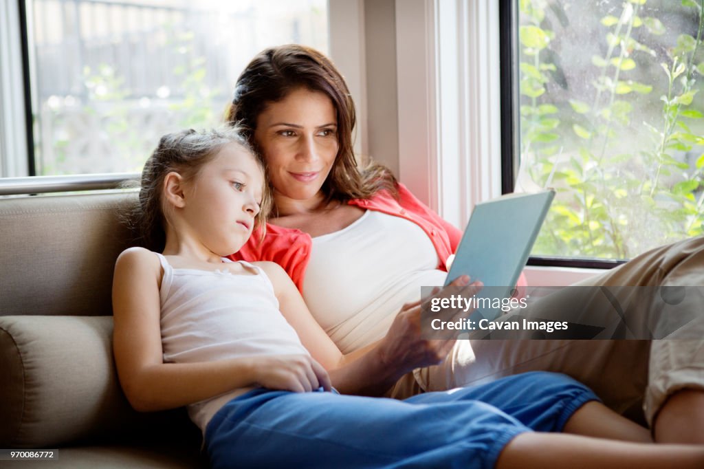 Woman teaching daughter while relaxing on sofa at home