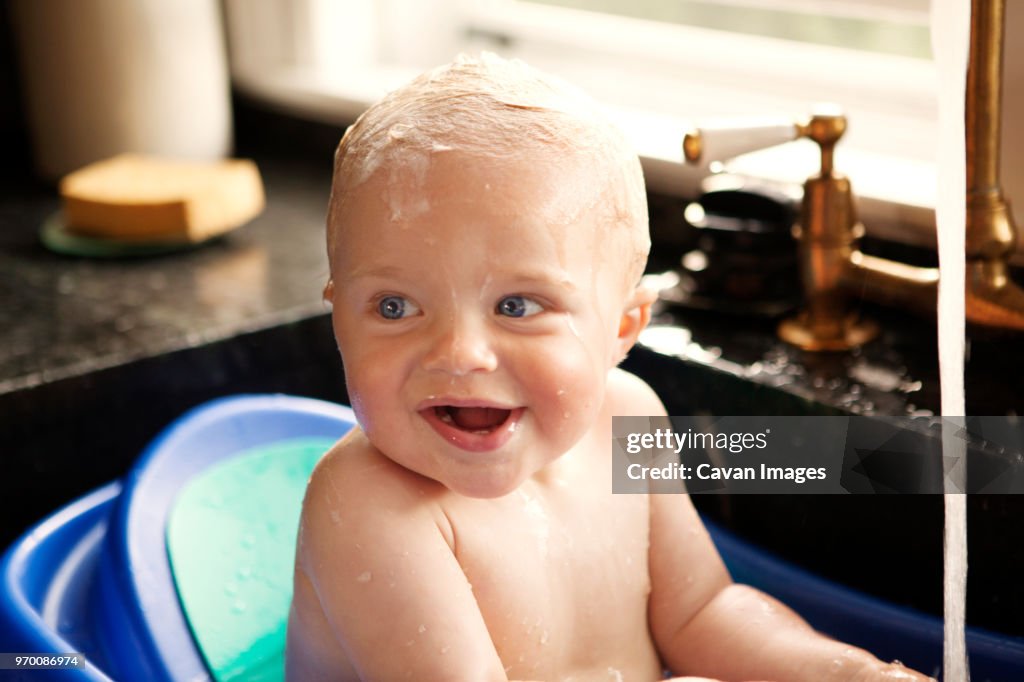 Happy baby boy looking away while bathing in kitchen sink