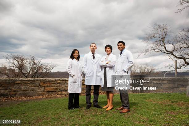 portrait of doctors standing on field against cloudy sky - four people stock pictures, royalty-free photos & images