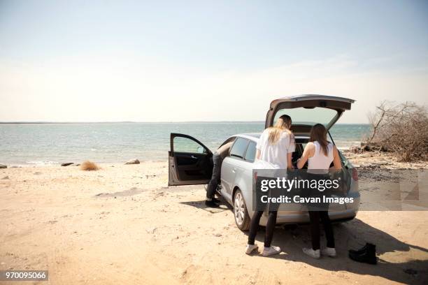 rear view of friends by car on shore at beach - boot stock pictures, royalty-free photos & images