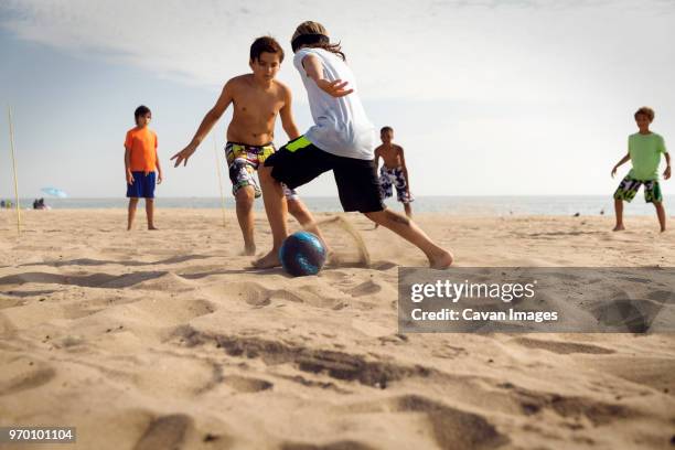friends playing soccer at beach against sea - boy barefoot rear view stockfoto's en -beelden