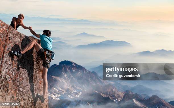 teamarbeit-paar helfende hand vertrauen inspirierende berge - caucasian mountain climber man stock-fotos und bilder